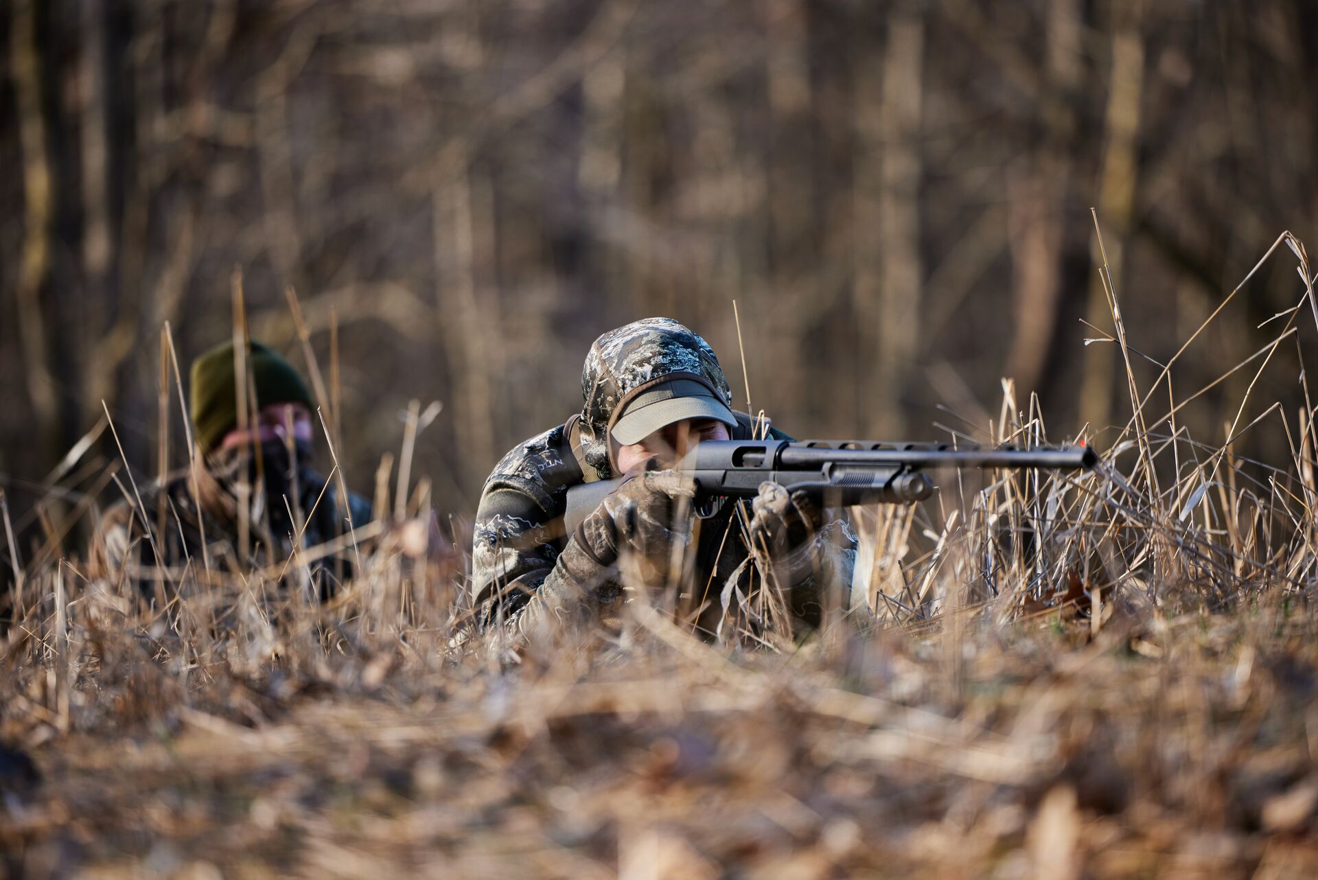 A hunter in camo aims a firearm while on the ground, know gun calibers for better hunting concept. 