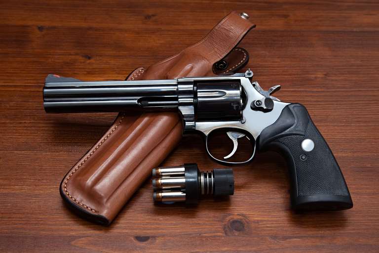 A revolver laying on a table and holster next to ammunition, understanding gun calibers concept. 