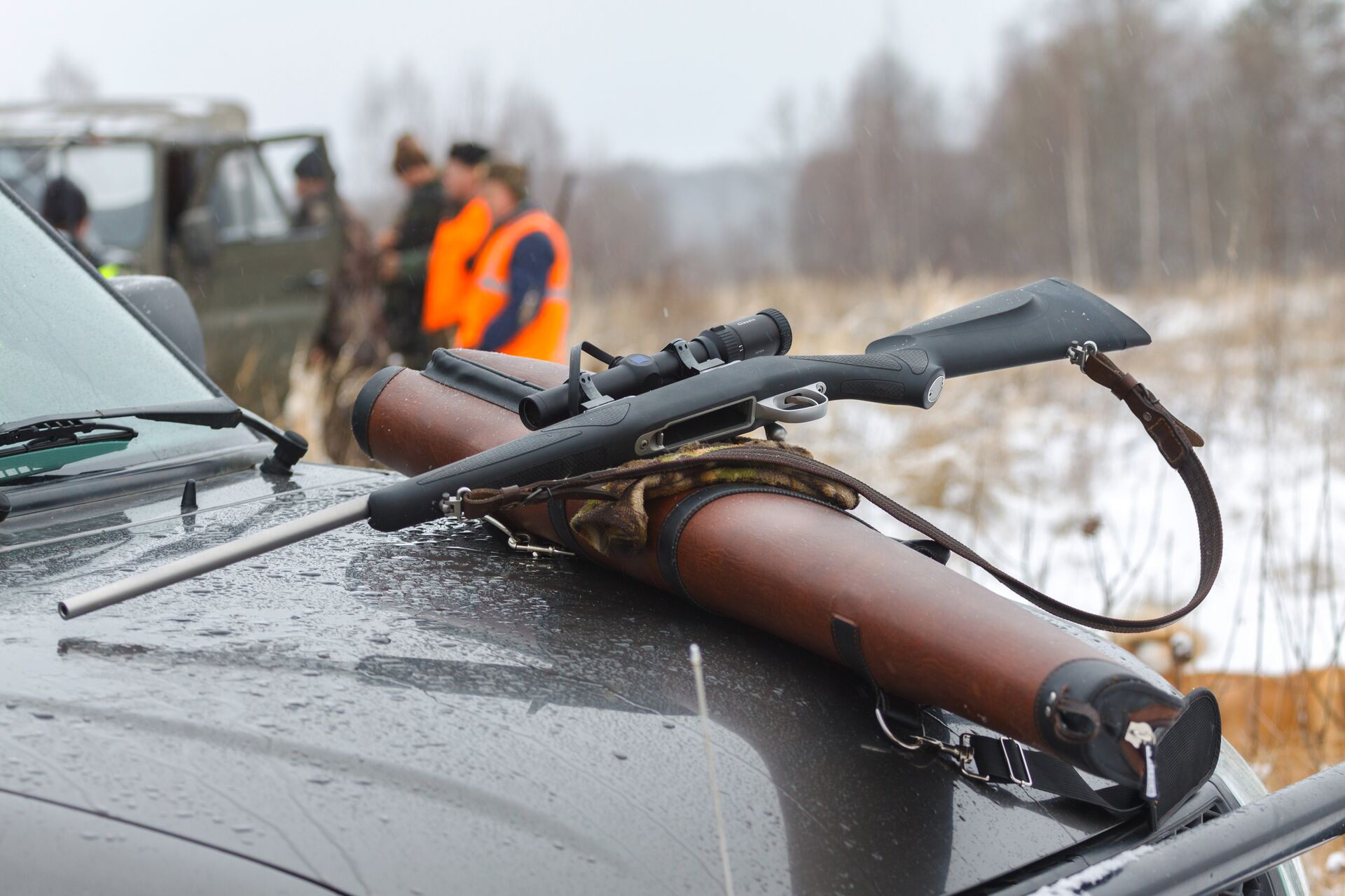 A rifle on the hood of a truck with hunters in the background, prepare for open season hunting concept. 