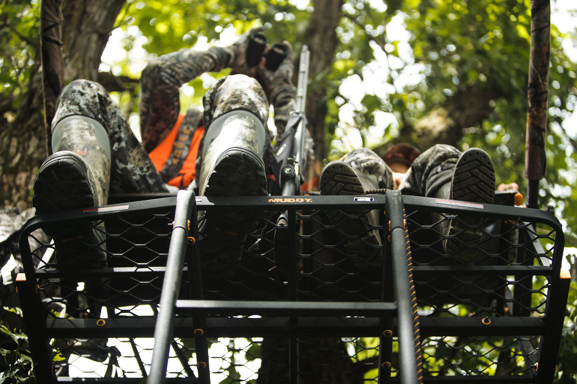 Two hunters sitting in a ladder stand in a tree. 