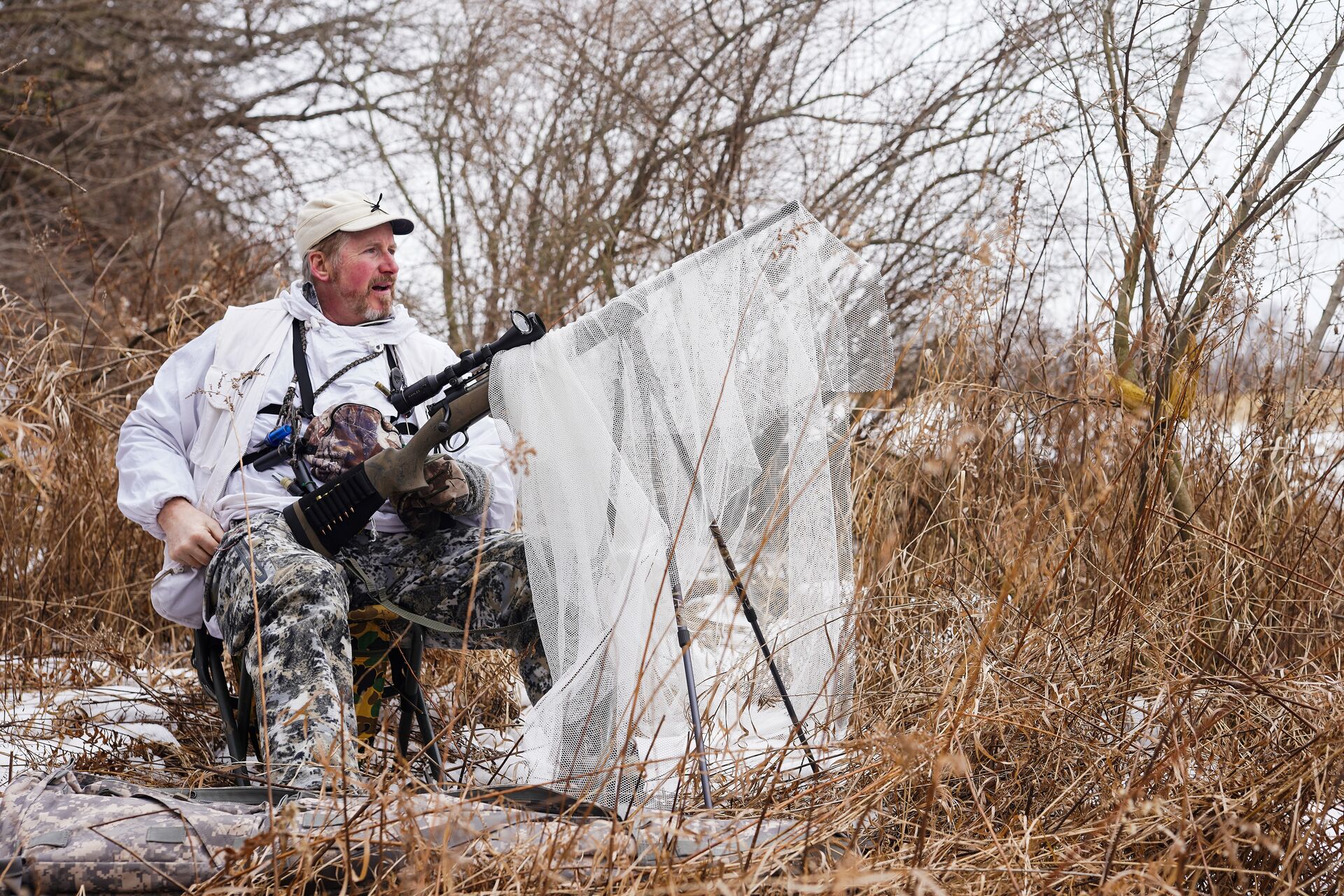 A coyote hunter set up with a rifle while wearing camo. 