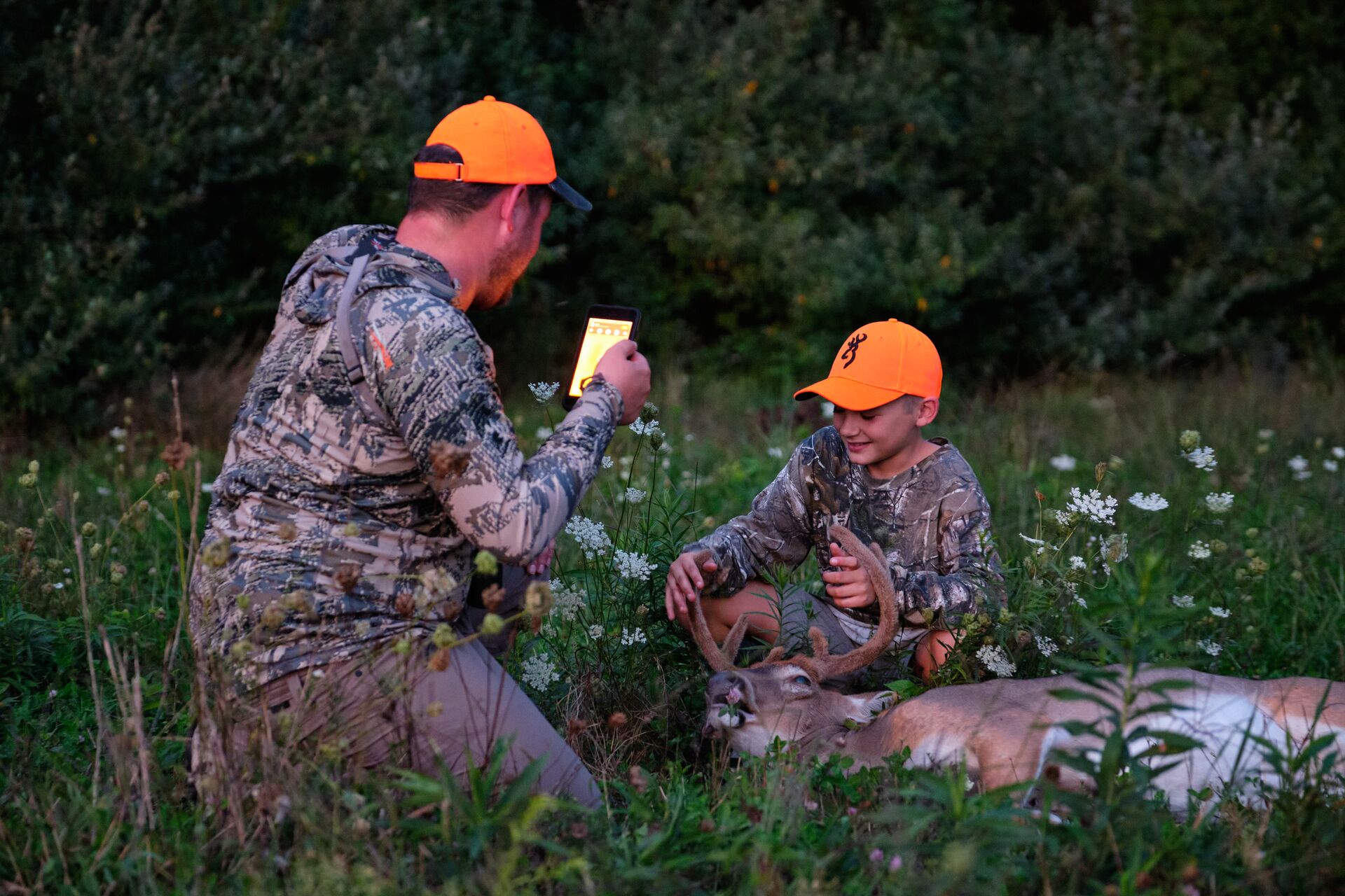 A man takes a picture of a young boy with his deer kill, youth hunting age concept. 