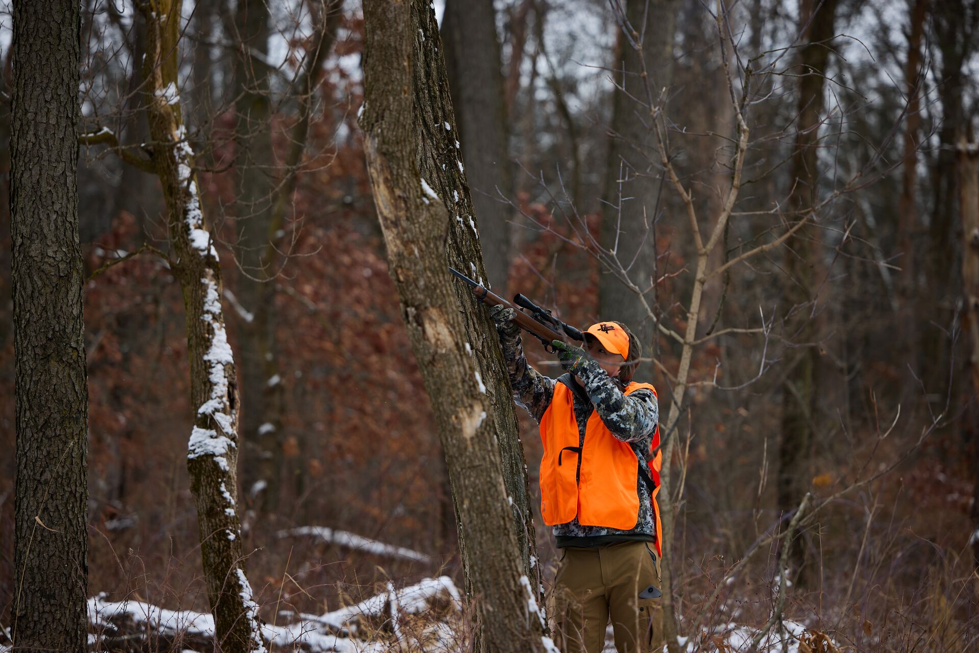 A hunter in blaze orange aims a rifle during a squirrel hunt. 