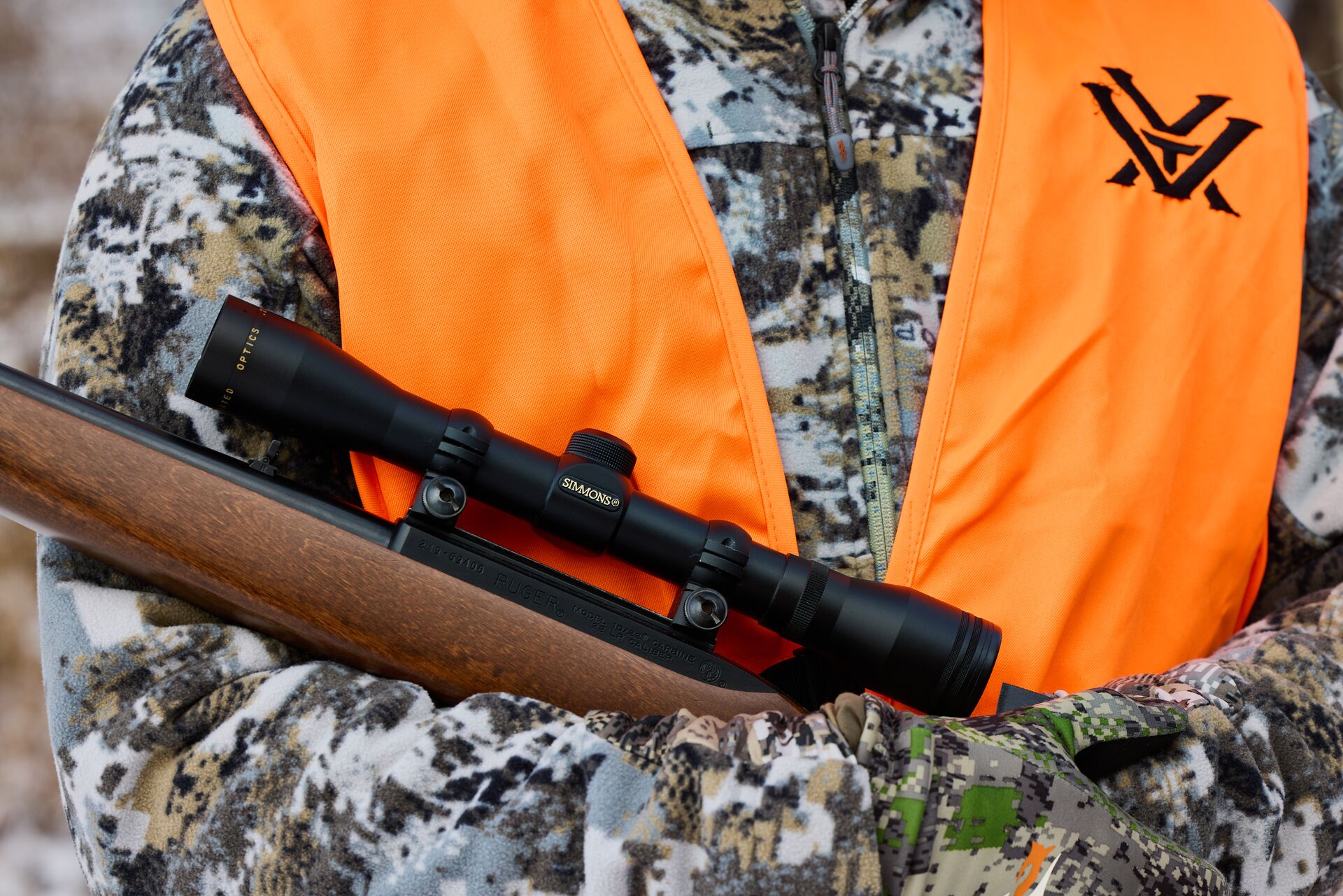 A hunter holds a rifle against an orange hunting vest, hunting license for squirrels concept. 