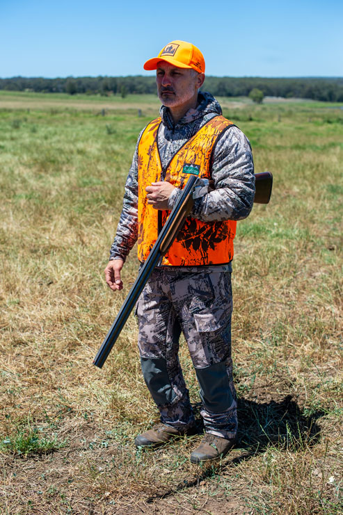 A hunter wearing blaze orange demonstrates the elbow carry. 